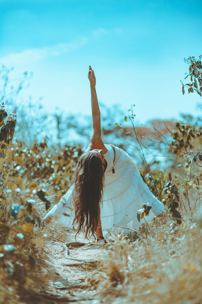 A woman practicing yoga in a peaceful, sunny outdoor setting surrounded by foliage.