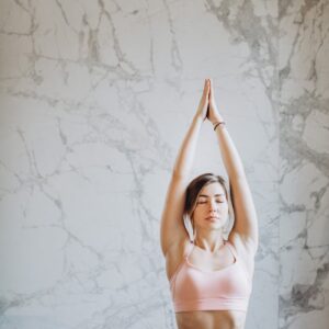 Young woman performing upward salute yoga pose indoors with marble background.