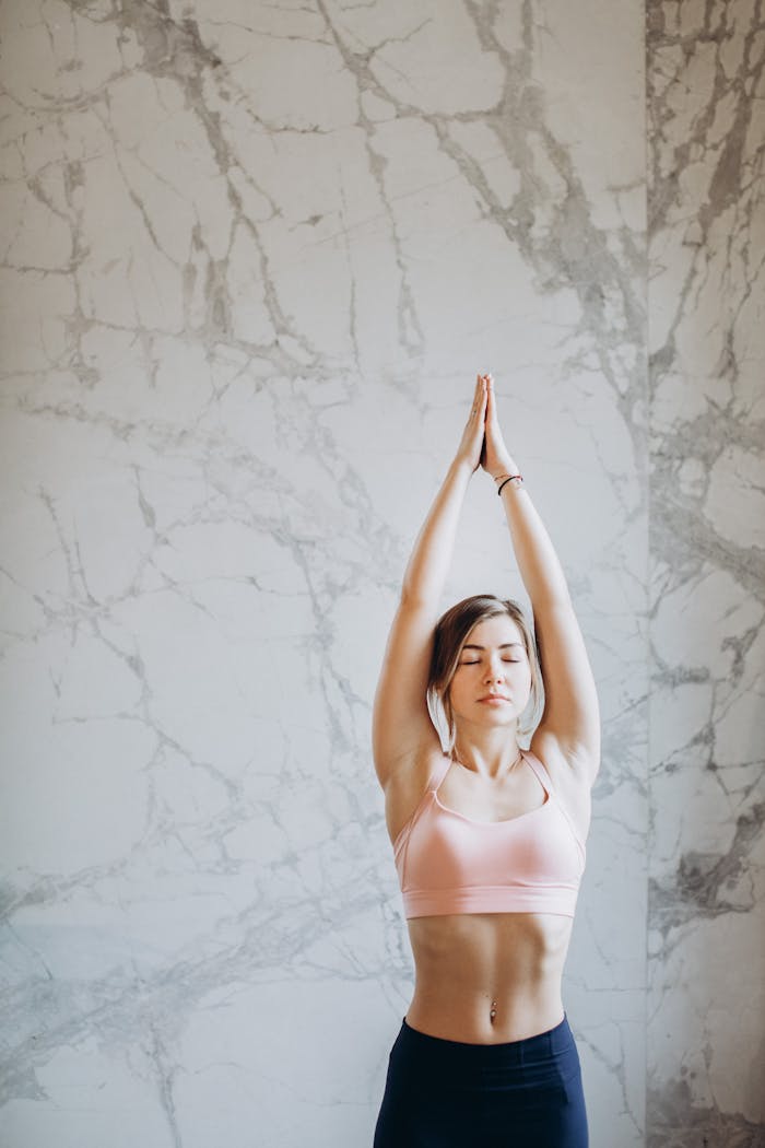 gallery-01 Young woman performing upward salute yoga pose indoors with marble background.